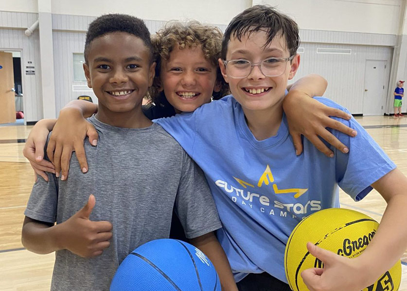 A group of three boys smiling confidently during an All Sports program at day camp