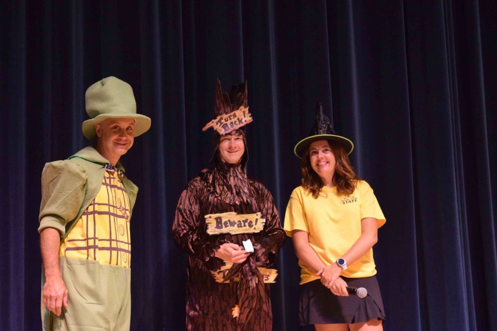 three adult camp counselors on stage during an arts performance, dressed up in costume